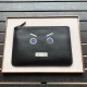 Clutch bag in plain calfskin leather decorated with a speechless emoticon in metal appliqué and logo on the back. 30 cm.