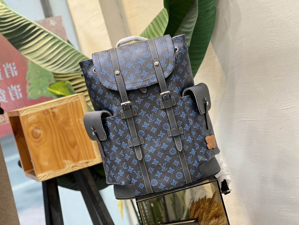 M46338 This Christopher MM backpack is made of coated canvas with a blue LV and Monogram floral pattern on a dark background. Finished with black leather trims and contrasting stitching, the bag is complemented by the LV