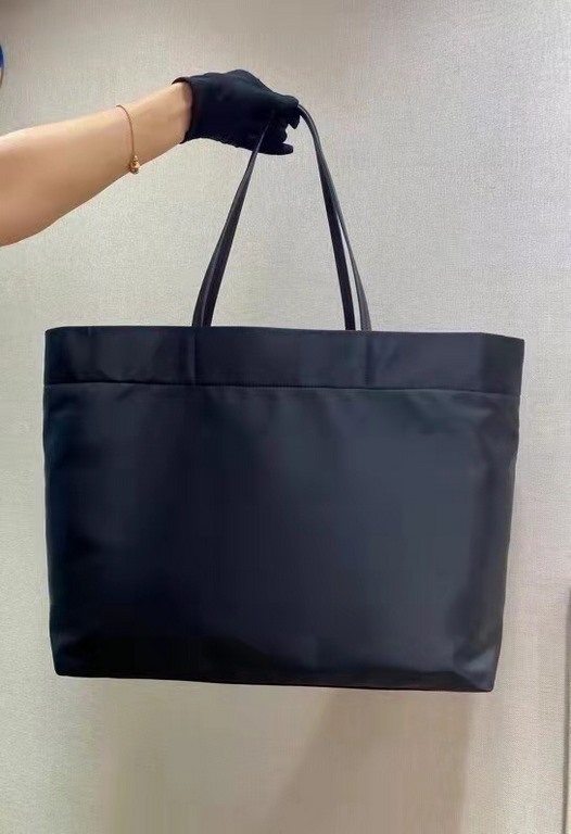 New Tote Bag 1BG107  This medium tote bag is crafted from innovative recycled nylon fabric for a minimalist and stylish design. Featuring a beautiful Saffiano leather carry handle, the bag is adorned with the iconic enam