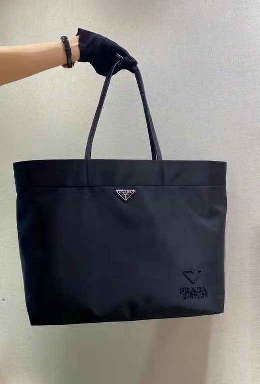 New Tote Bag 1BG107  This medium tote bag is crafted from innovative recycled nylon fabric for a minimalist and stylish design. Featuring a beautiful Saffiano leather carry handle, the bag is adorned with the iconic enam