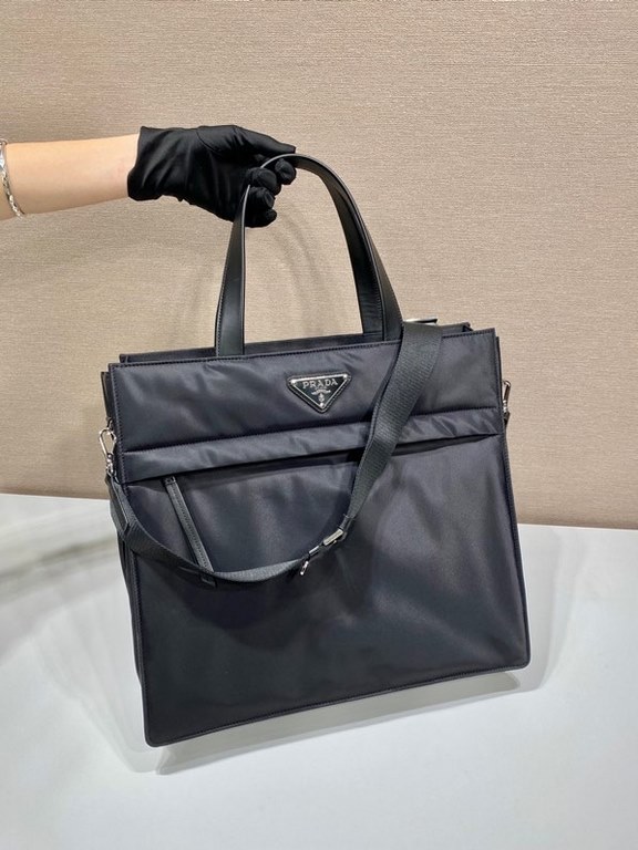 Upgraded Tote Bag 2VG076This tote bag presents a compact square design adorned with leather details. The iconic enameled triangle logo on the front emphasizes the brand's style. Fitted with a long detachable shoulder str