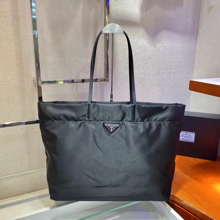 New Tote Bag 1BG107  This medium tote bag is crafted from innovative recycled nylon fabric for a minimalist and stylish design. Featuring a beautiful Saffiano leather carry handle, the bag is adorned with the iconic enam